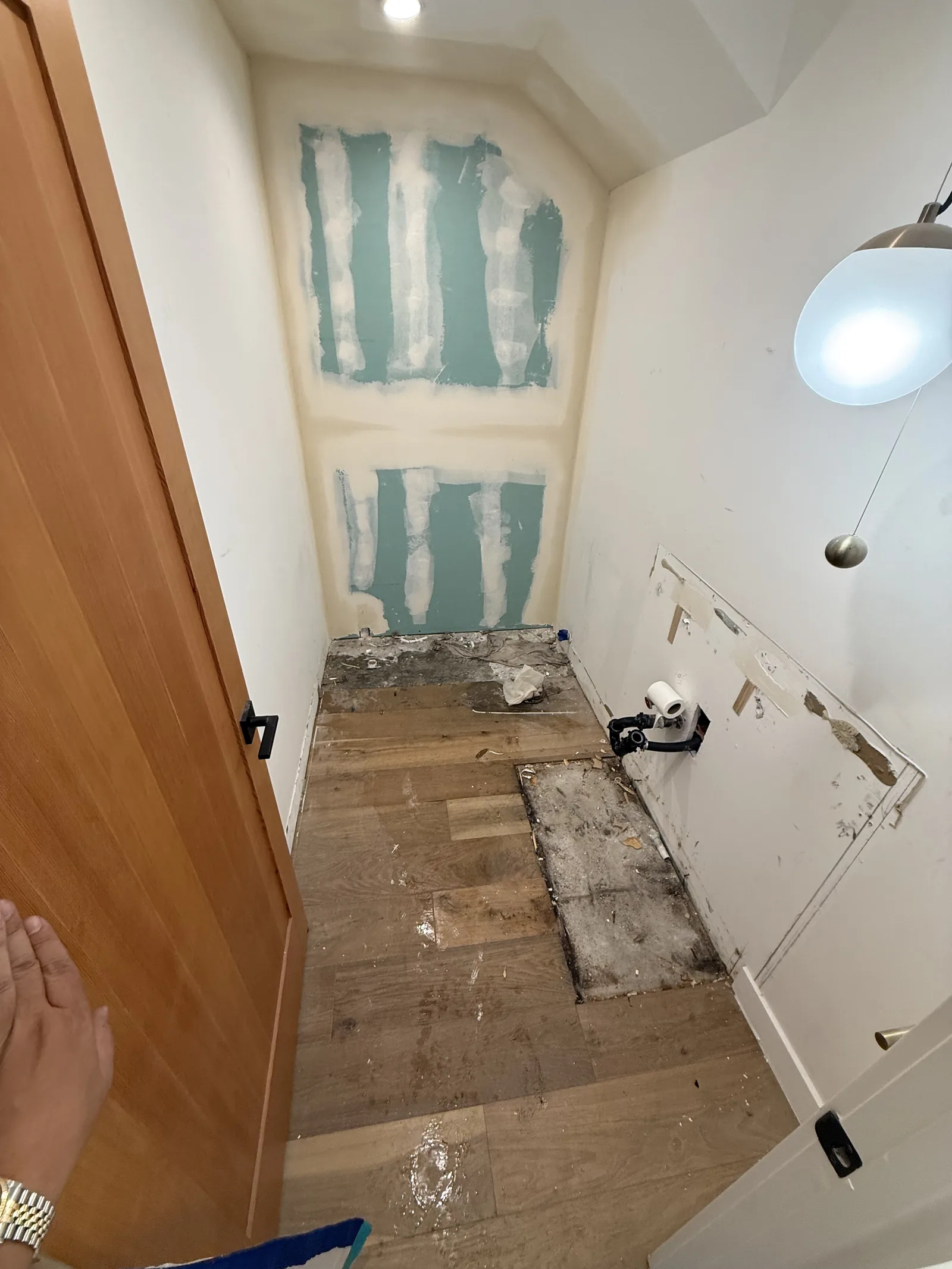 An interior wall opened near a doorway, with warped wood flooring showing water damage