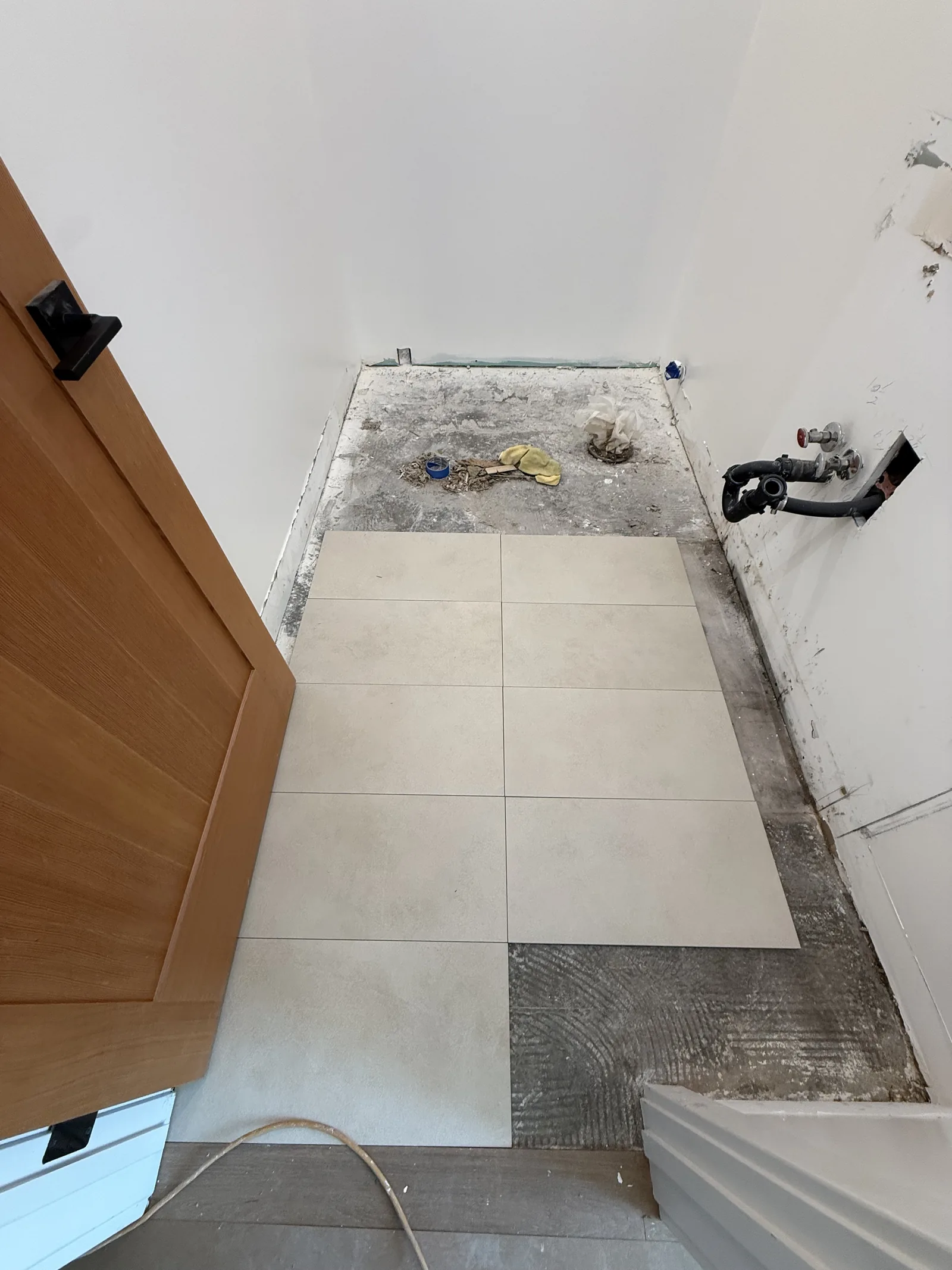 A small interior room with new tile partially laid and plumbing rough-in visible