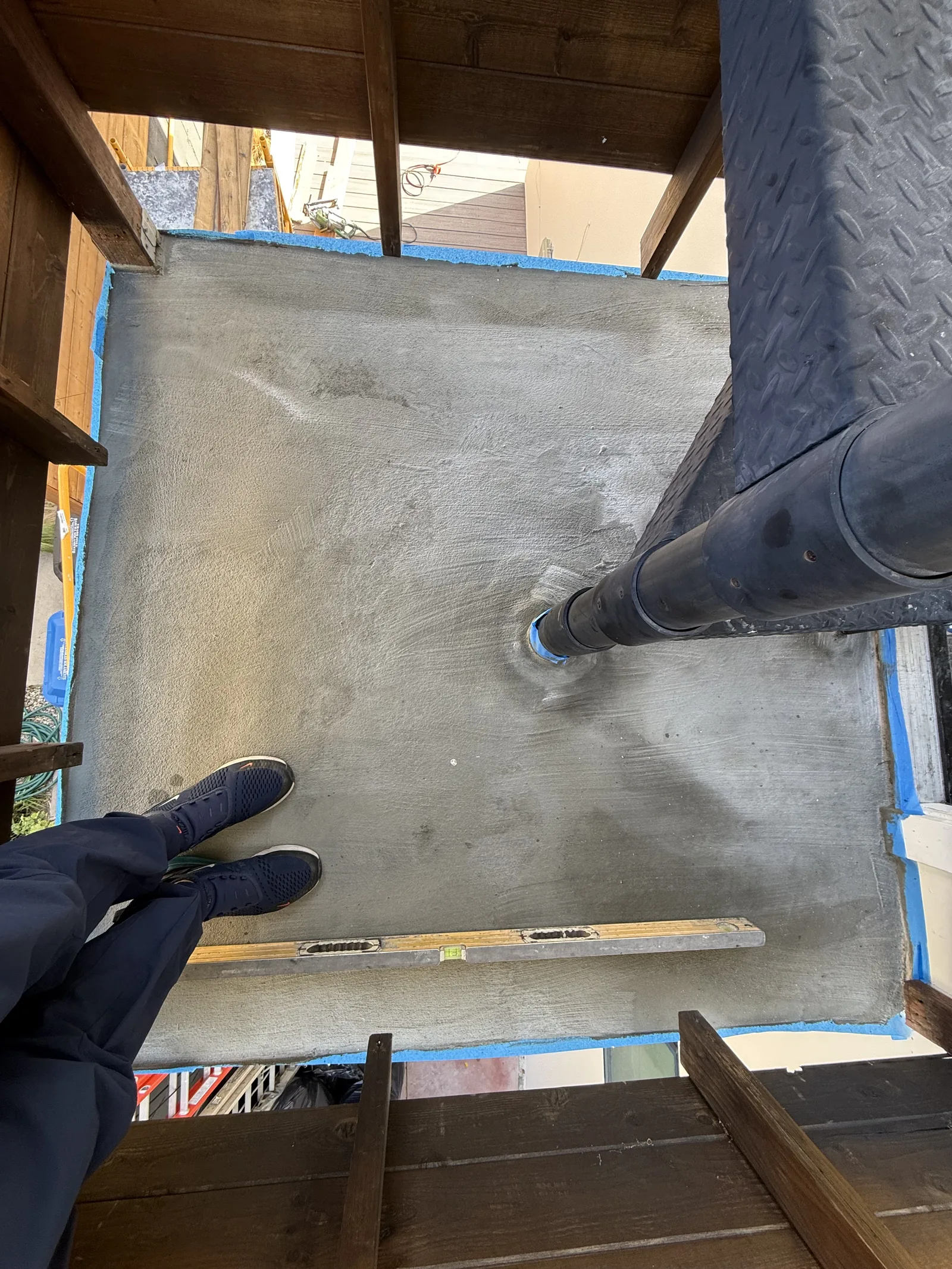 A waterproofed stair landing checked for slope with a level, with the new downspout routed through it