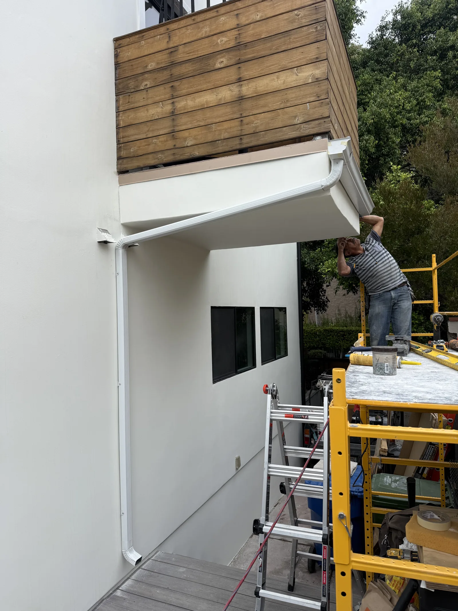 A worker installing the new white rain gutter along the underside of the rebuilt balcony