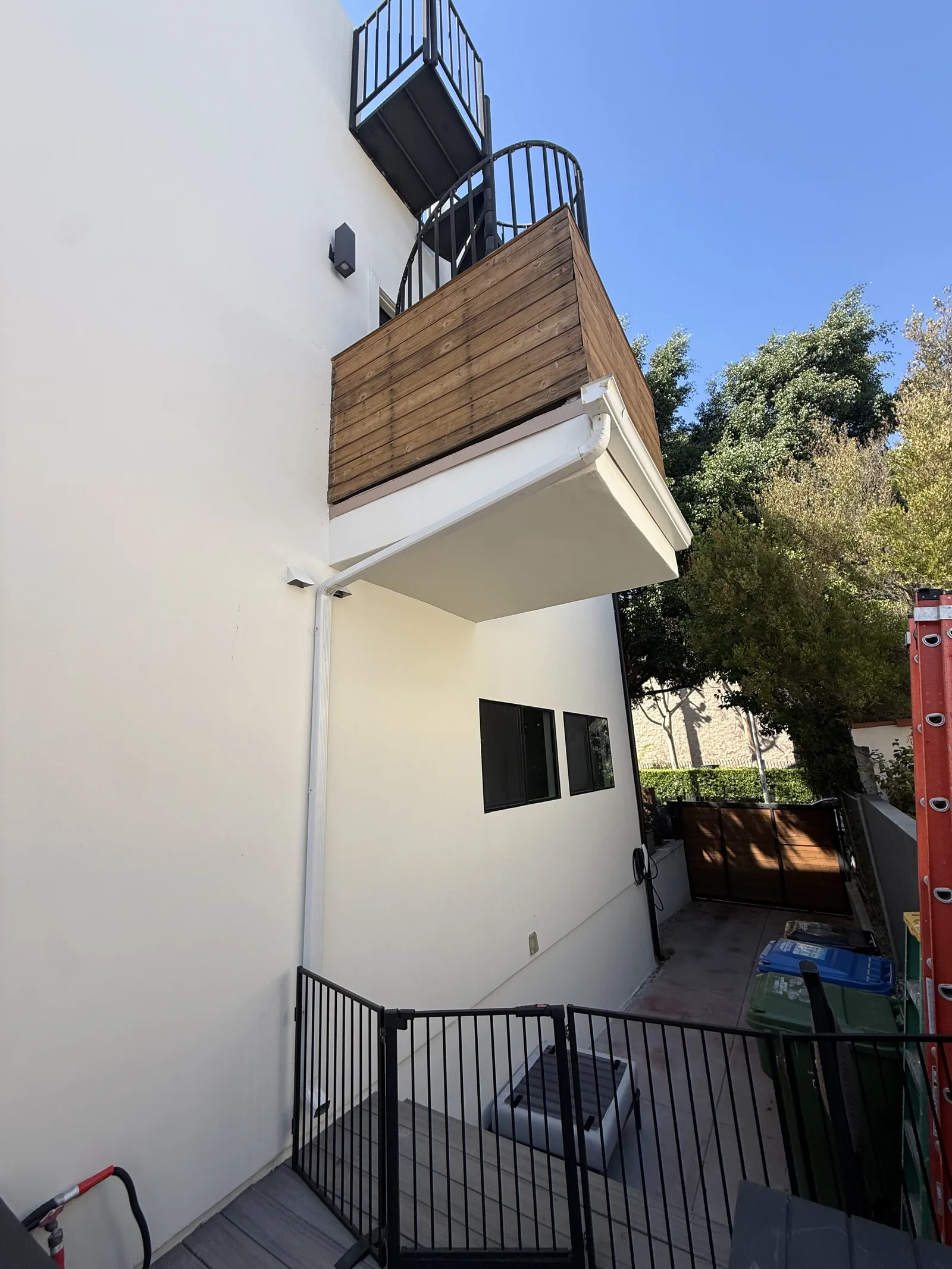 A finished second-floor balcony with new wood cladding and a rain gutter, and a black spiral staircase