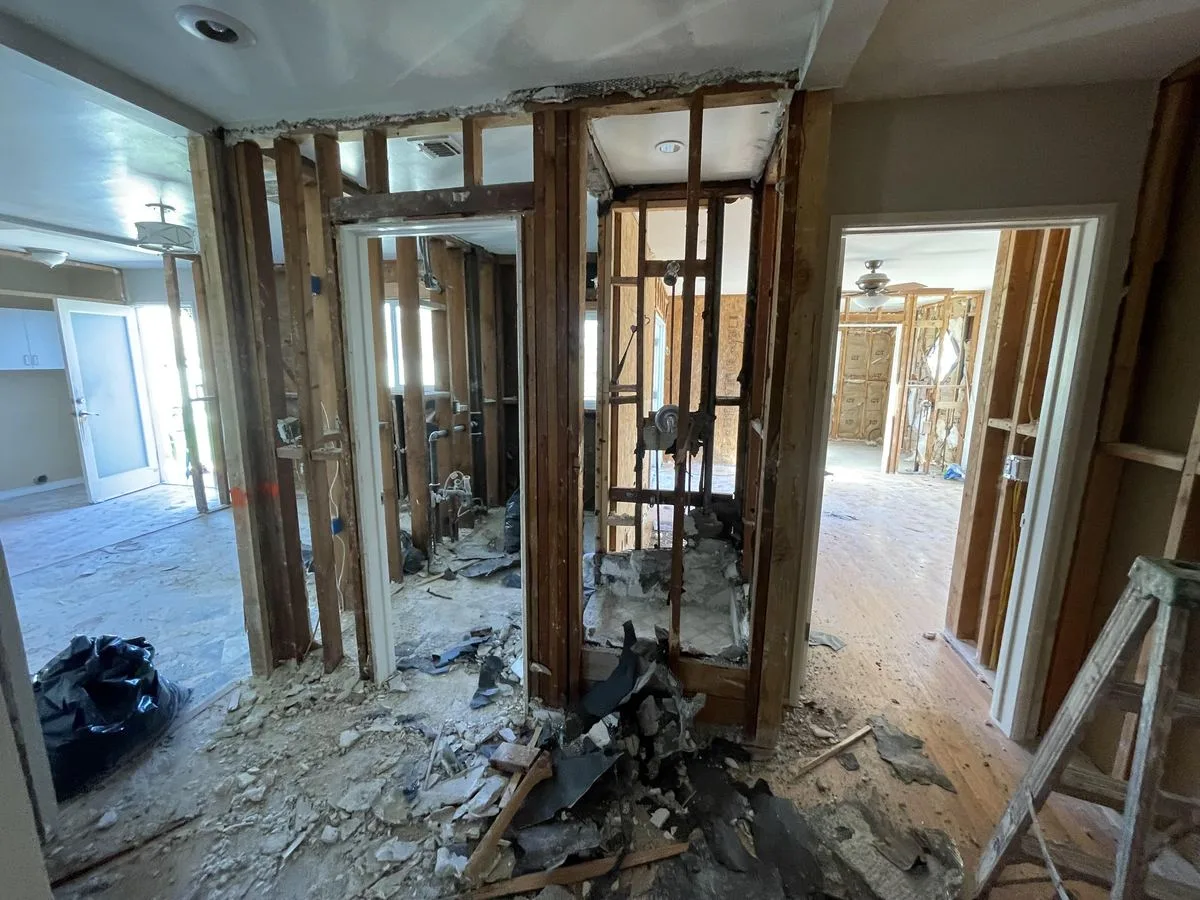 A room opened to bare stud framing with brick and plaster debris piled on the floor