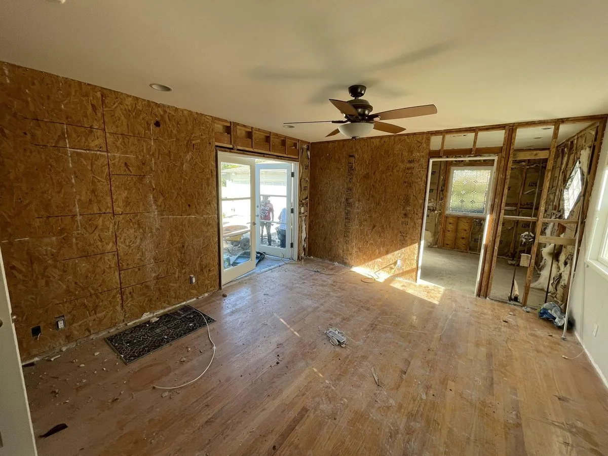 An empty room with new plywood subfloor and OSB wall sheathing, ceiling fan overhead