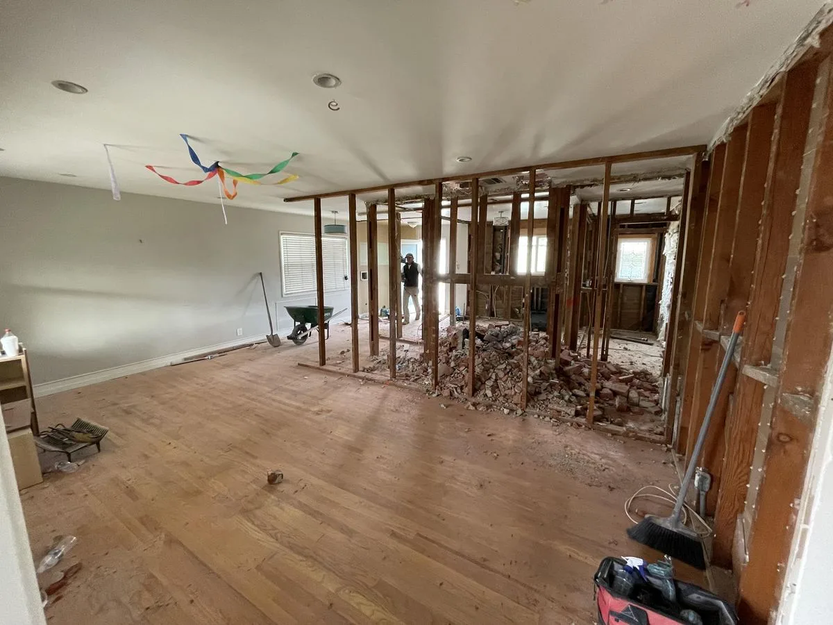 An open floor plan room with a framed wall opening and a worker visible through it