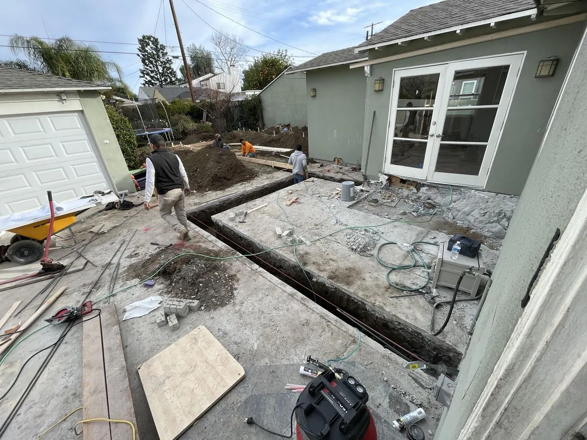 A wide exterior view of a house with a foundation trench and slab under construction in the backyard