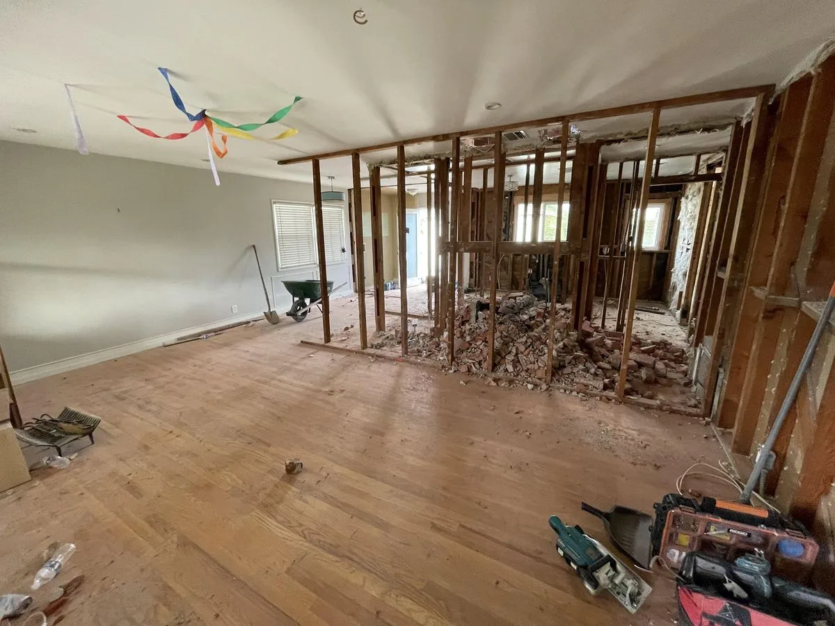 An open room with exposed stud framing and demolition tools on the floor