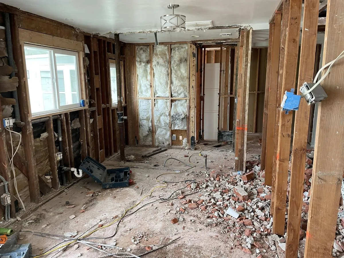 An interior wall opened to the studs with fiberglass insulation and brick debris exposed
