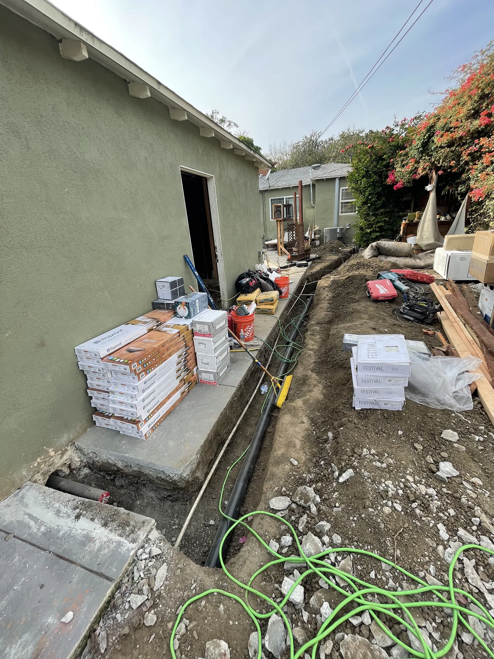 A utility trench along the side yard, with pipe and tile stacked nearby
