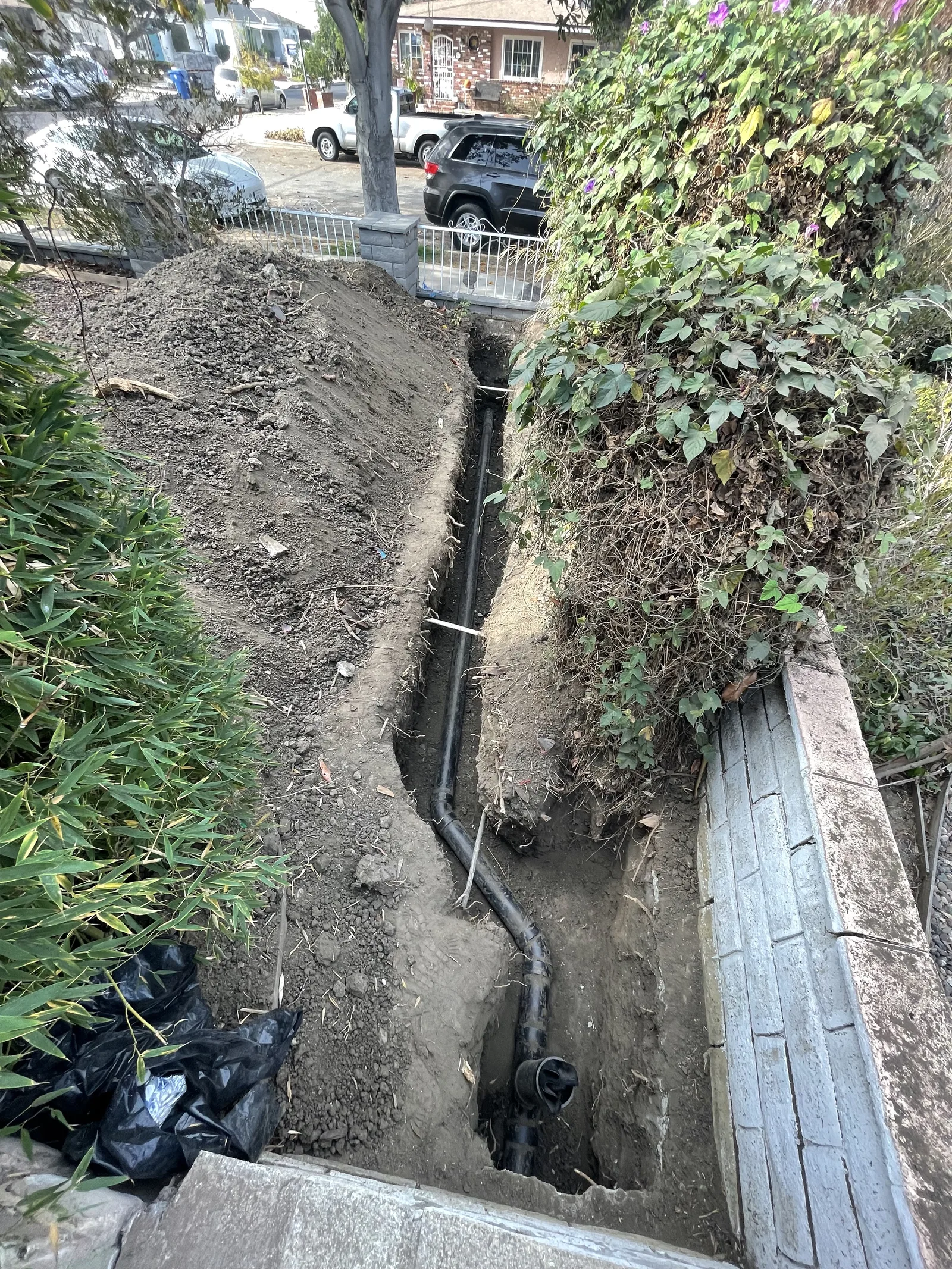 A utility trench continuing toward the front of a property, with parked cars visible at street level