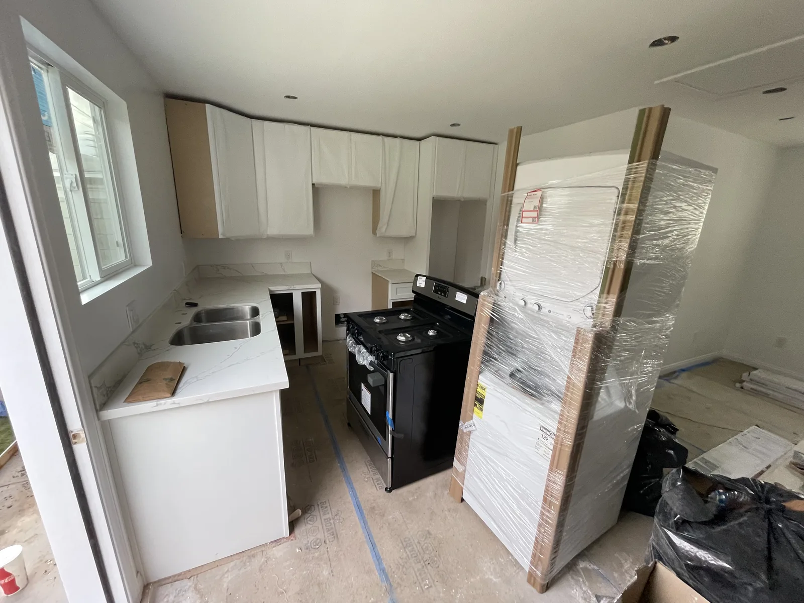 A kitchen with white cabinets, countertop, and a range installed, with a wrapped refrigerator