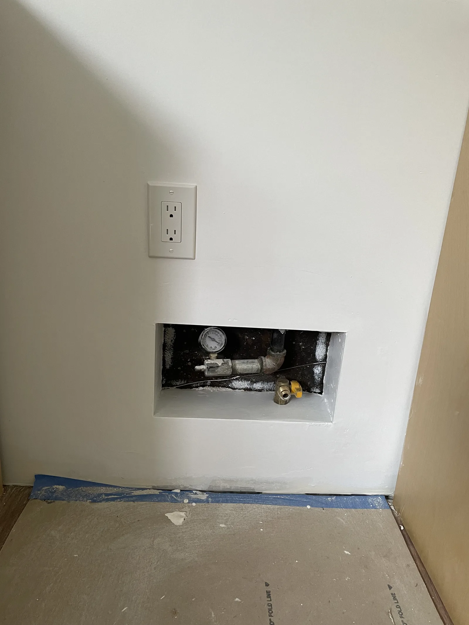 A laundry hookup nook with an electrical outlet and plumbing valves in the wall