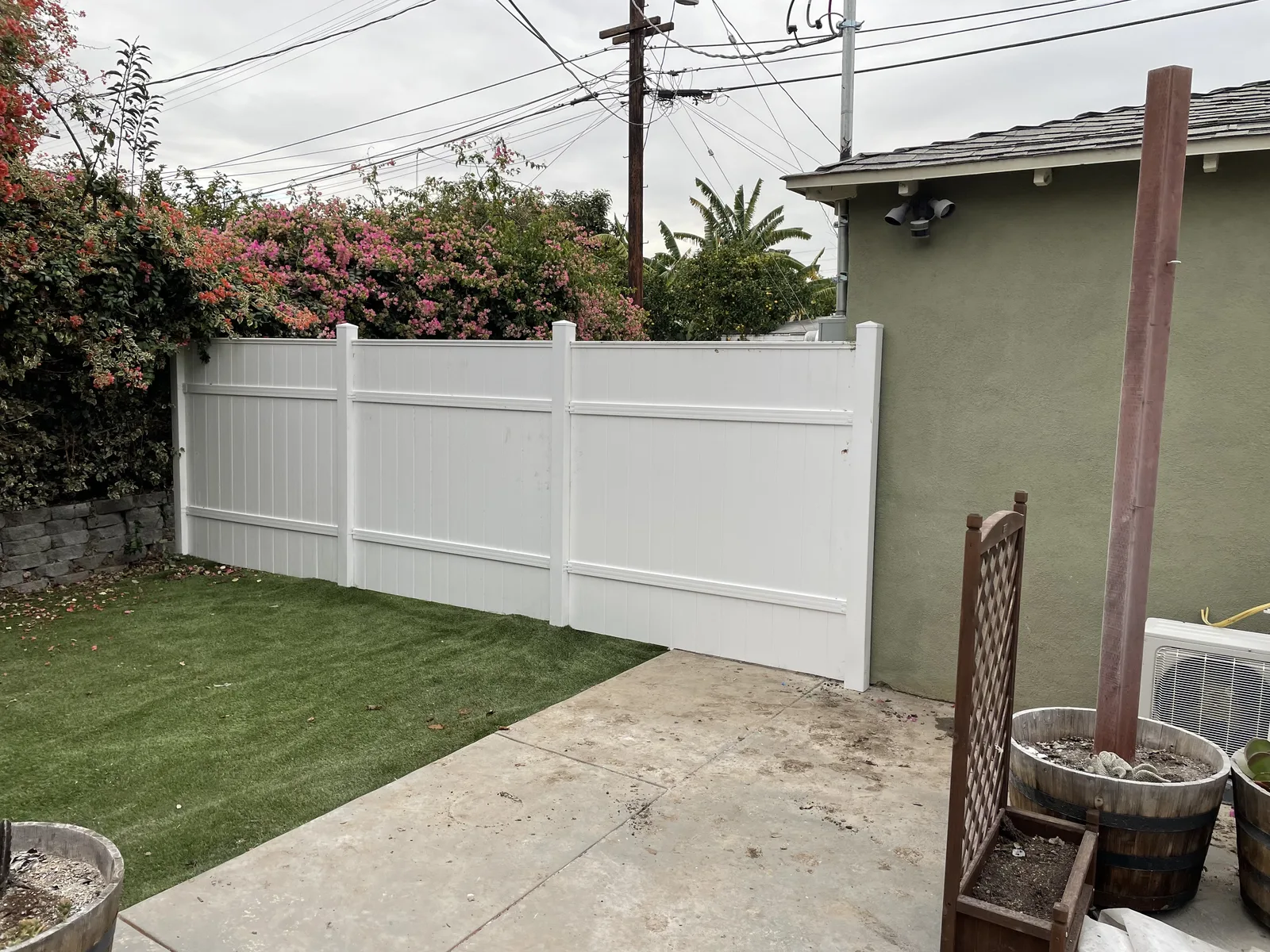 A new white vinyl fence dividing a backyard, with artificial turf on one side
