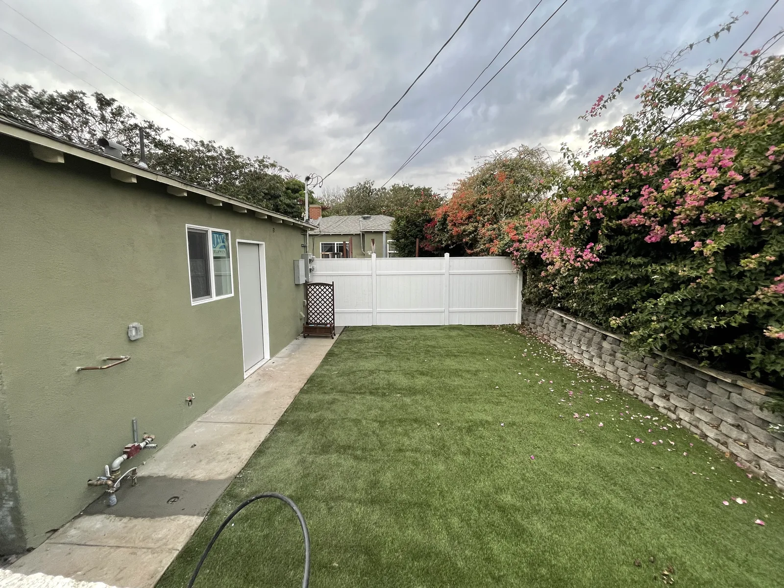 A backyard fence and lawn, with another house visible beyond it
