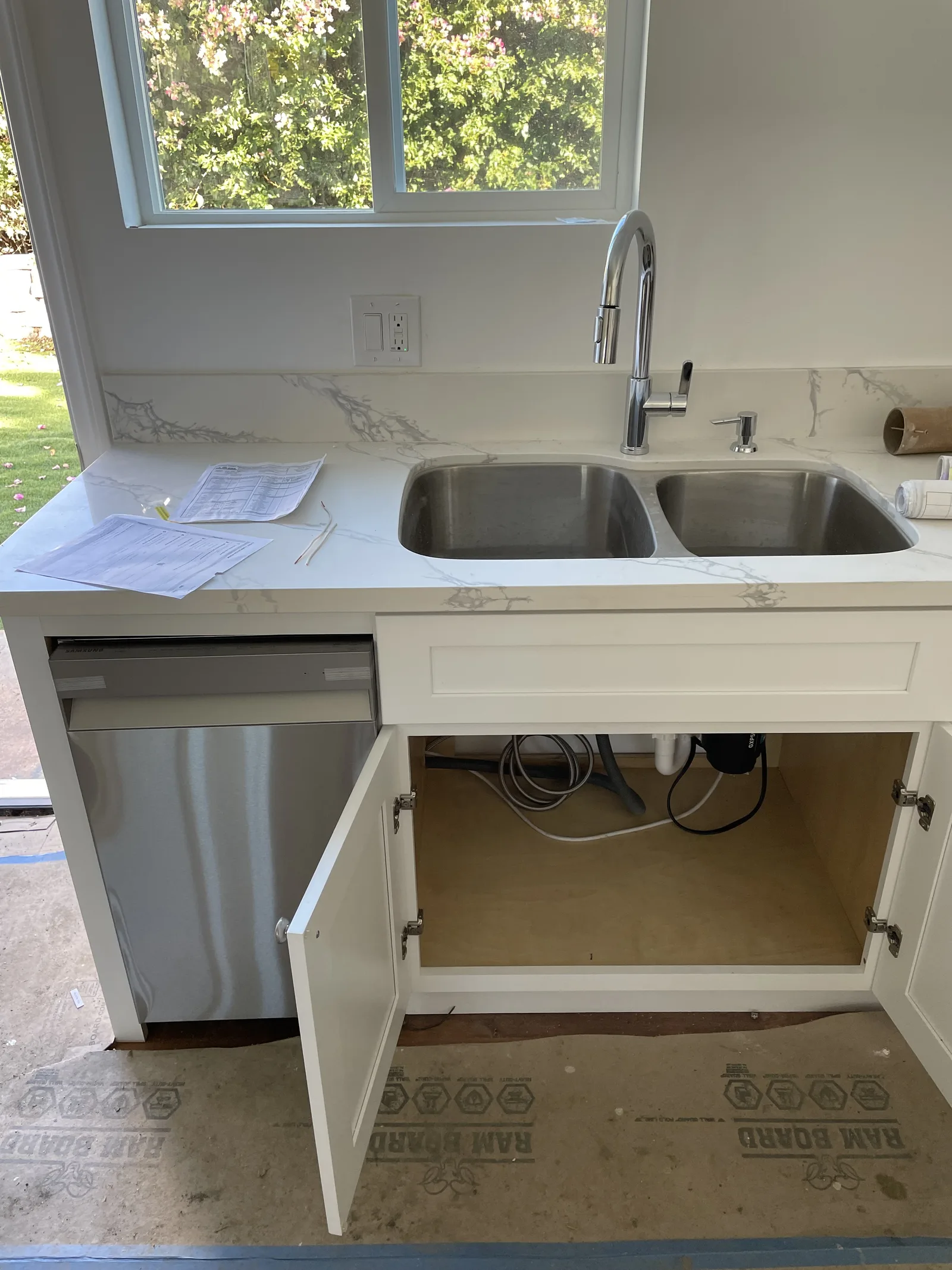 A kitchen sink and faucet installed, with the cabinet doors below open