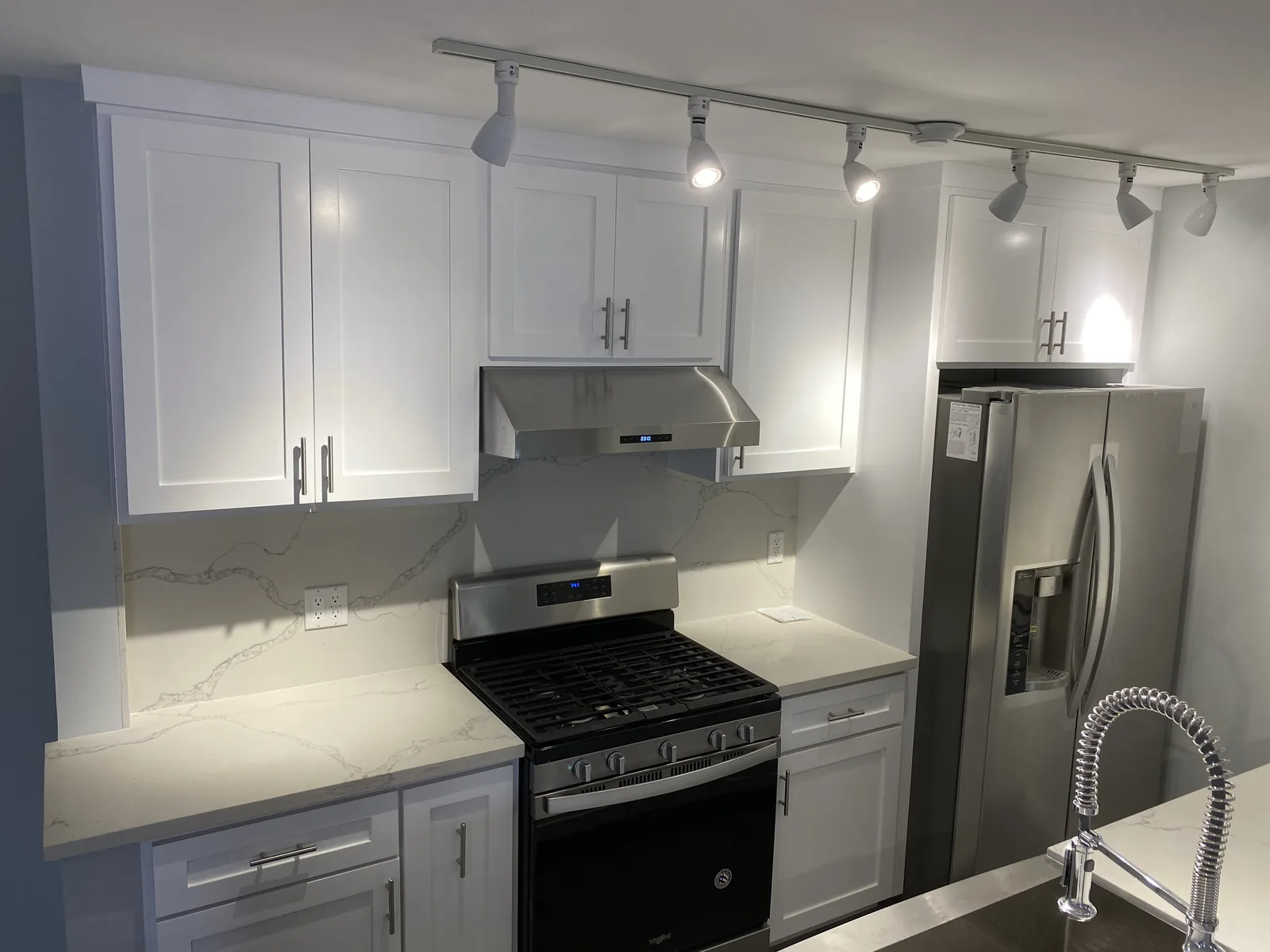 The finished kitchen with white shaker cabinets, quartz counters, and stainless appliances
