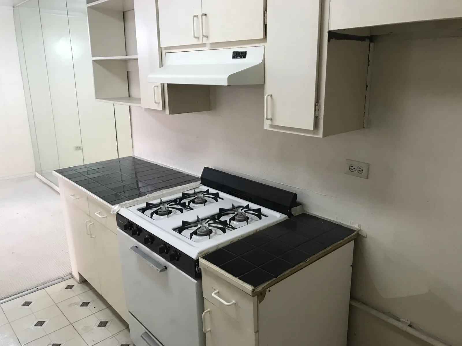 The original kitchen before the remodel, with cream cabinets, a black tile countertop, and an old white gas range