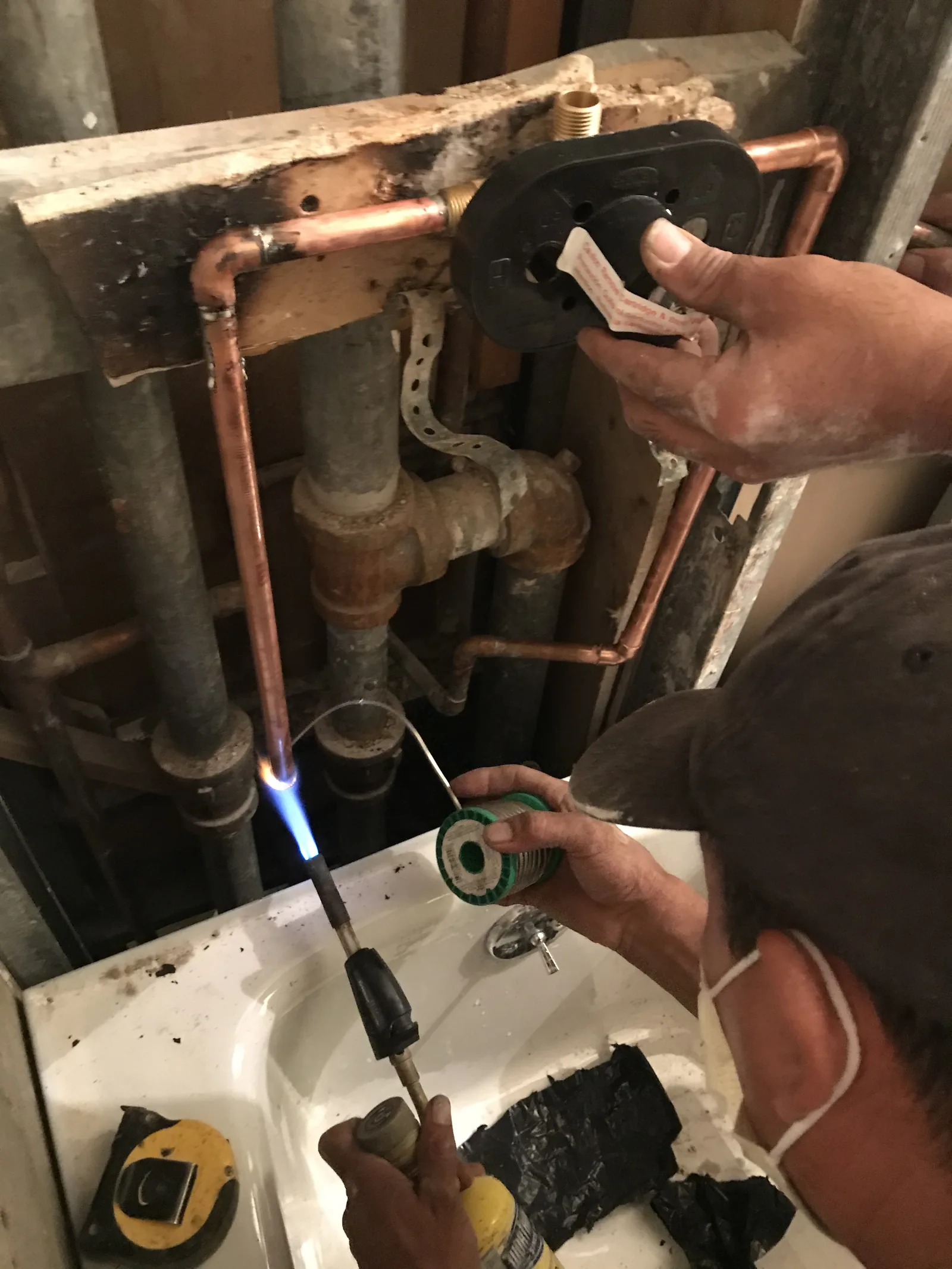 A plumber sweat-soldering a copper pipe joint with a torch inside an open wall