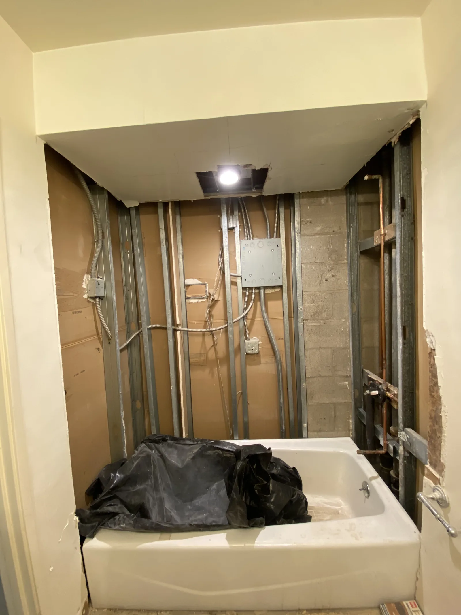 A bathtub set in place with rough framing and an electrical box on the wall beside it
