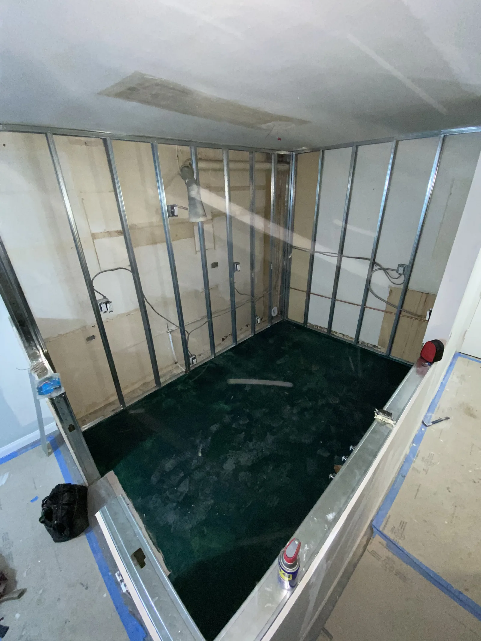 A new walk-in shower stall framed in metal studs with the pan waterproofed in a teal membrane