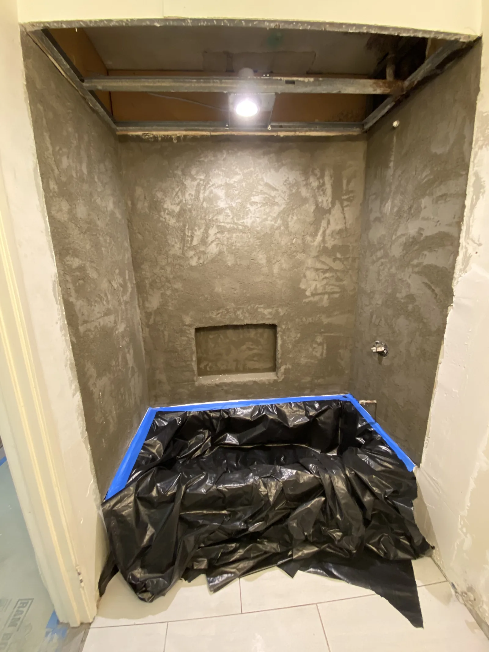 A shower stall with a scratch-coat mortar bed on the walls, ready for tile, and the pan protected with plastic sheeting