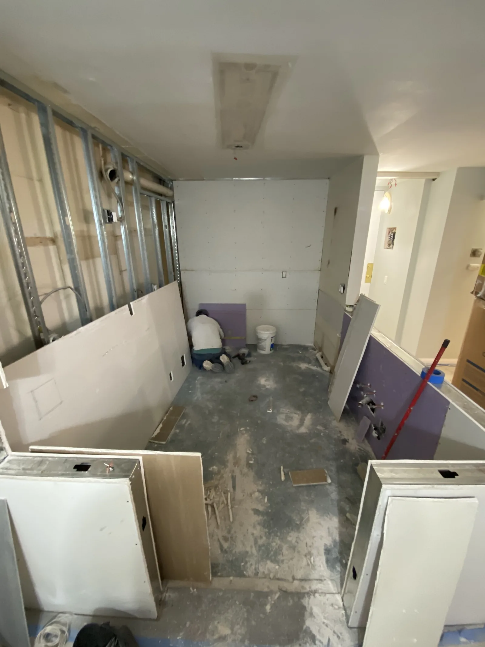 The second bathroom with new drywall installed and a worker setting the toilet in place