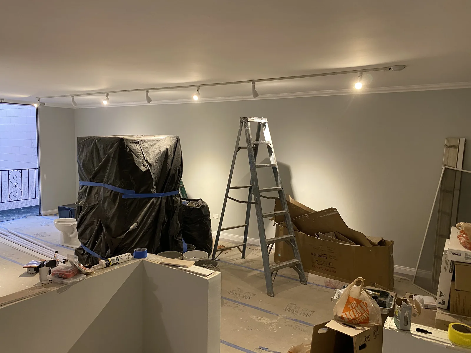 A living room with furniture covered in plastic sheeting and a ladder set up for painting