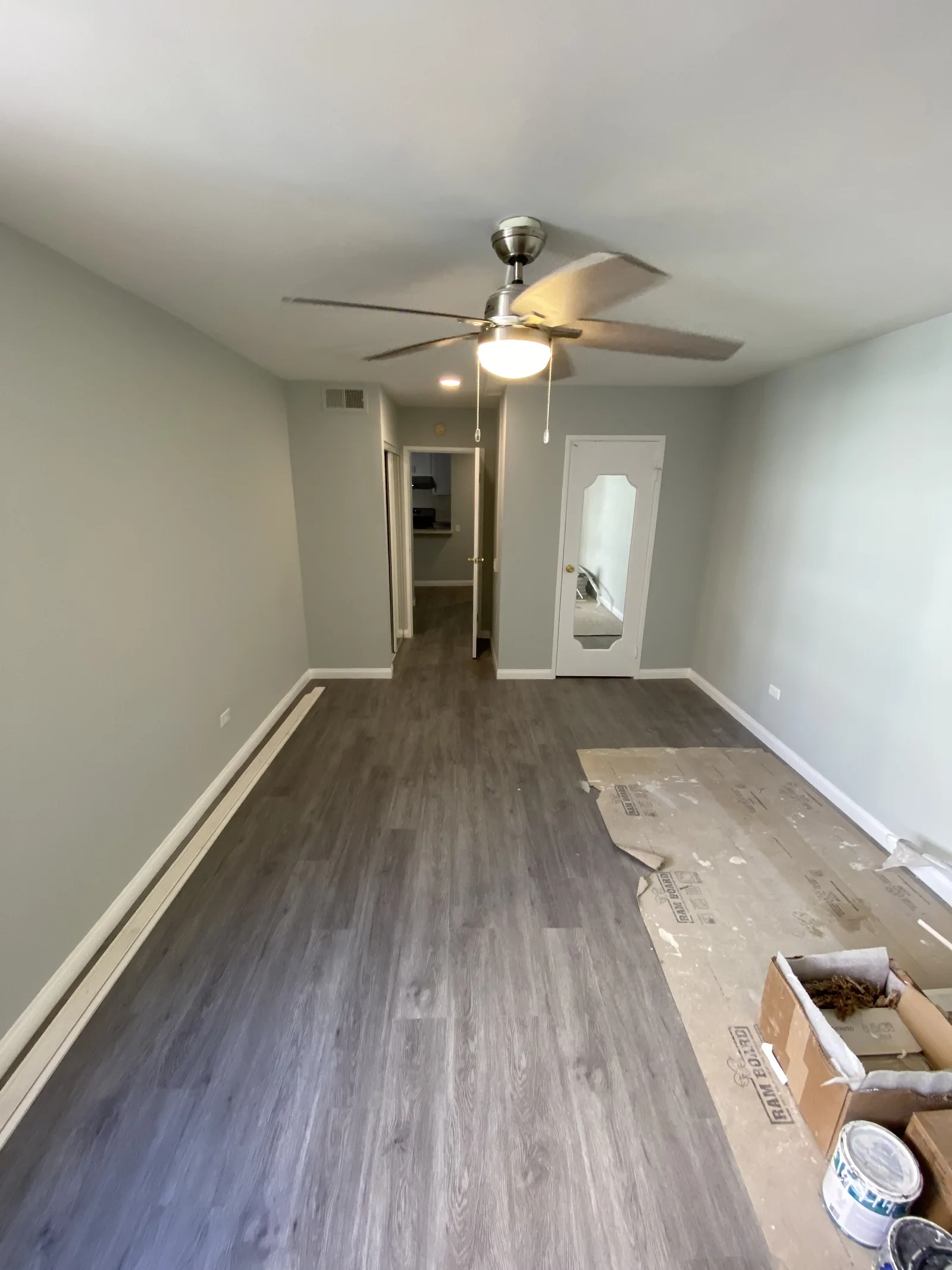 A hallway with new flooring, new baseboards, and a ceiling fan visible ahead