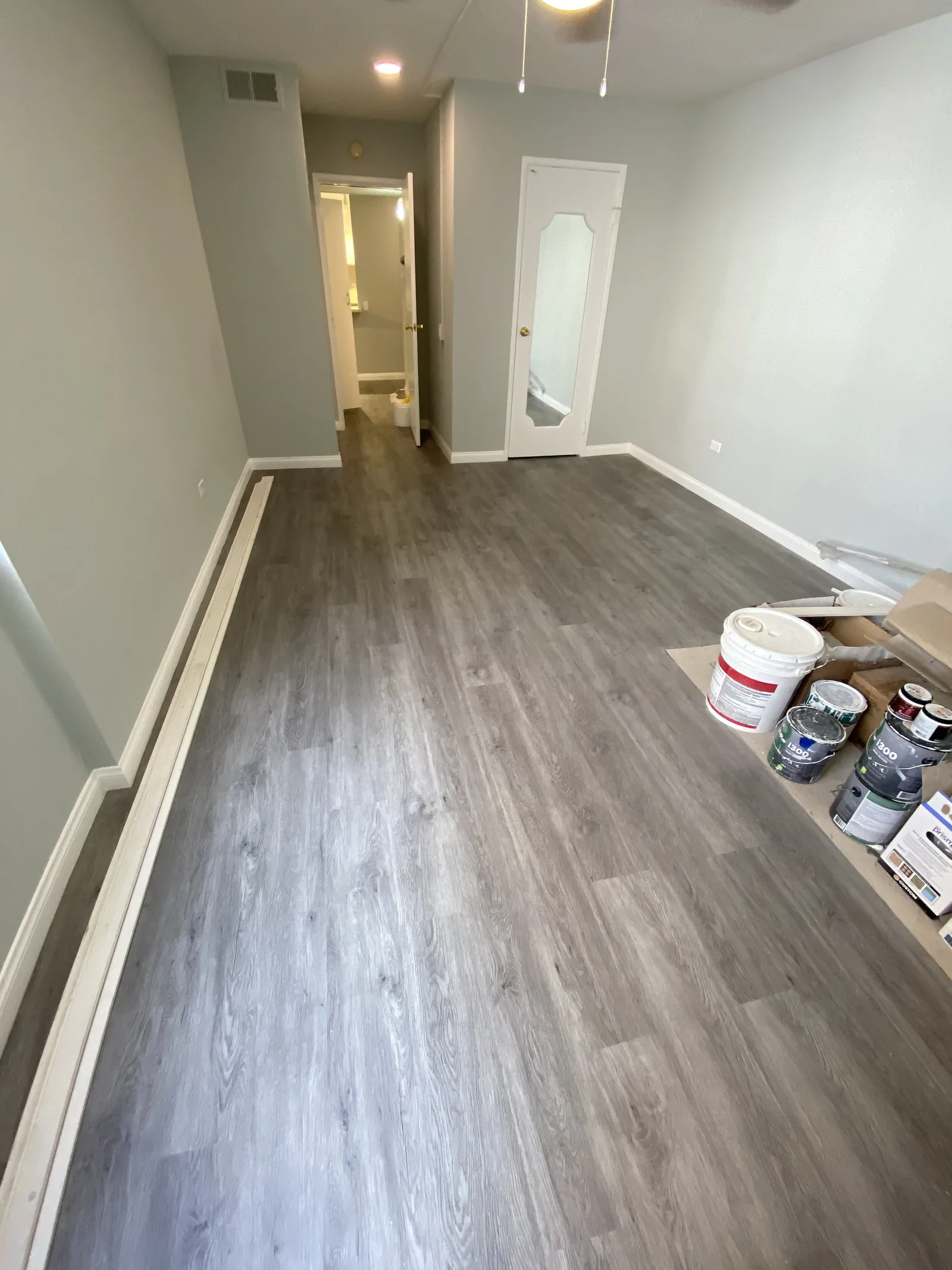 A bedroom with new flooring and fresh paint complete, with paint supplies still staged for touch-ups