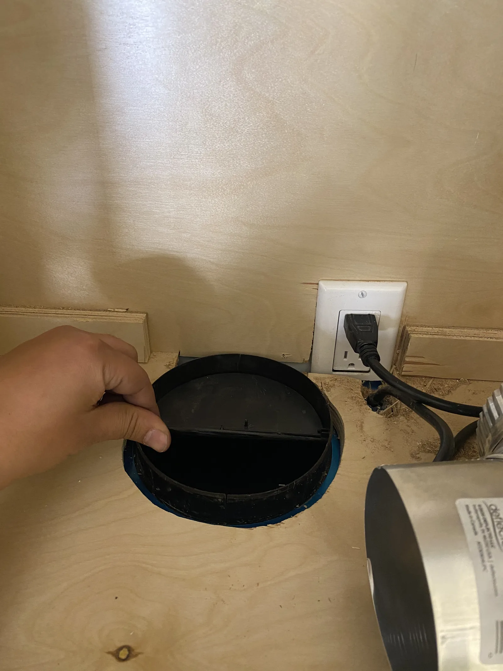 A wire pass-through grommet installed in the back of a cabinet next to an outlet