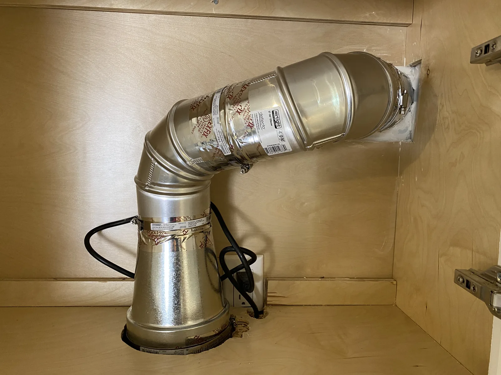 A range hood exhaust duct routed through a cabinet to a new wall vent
