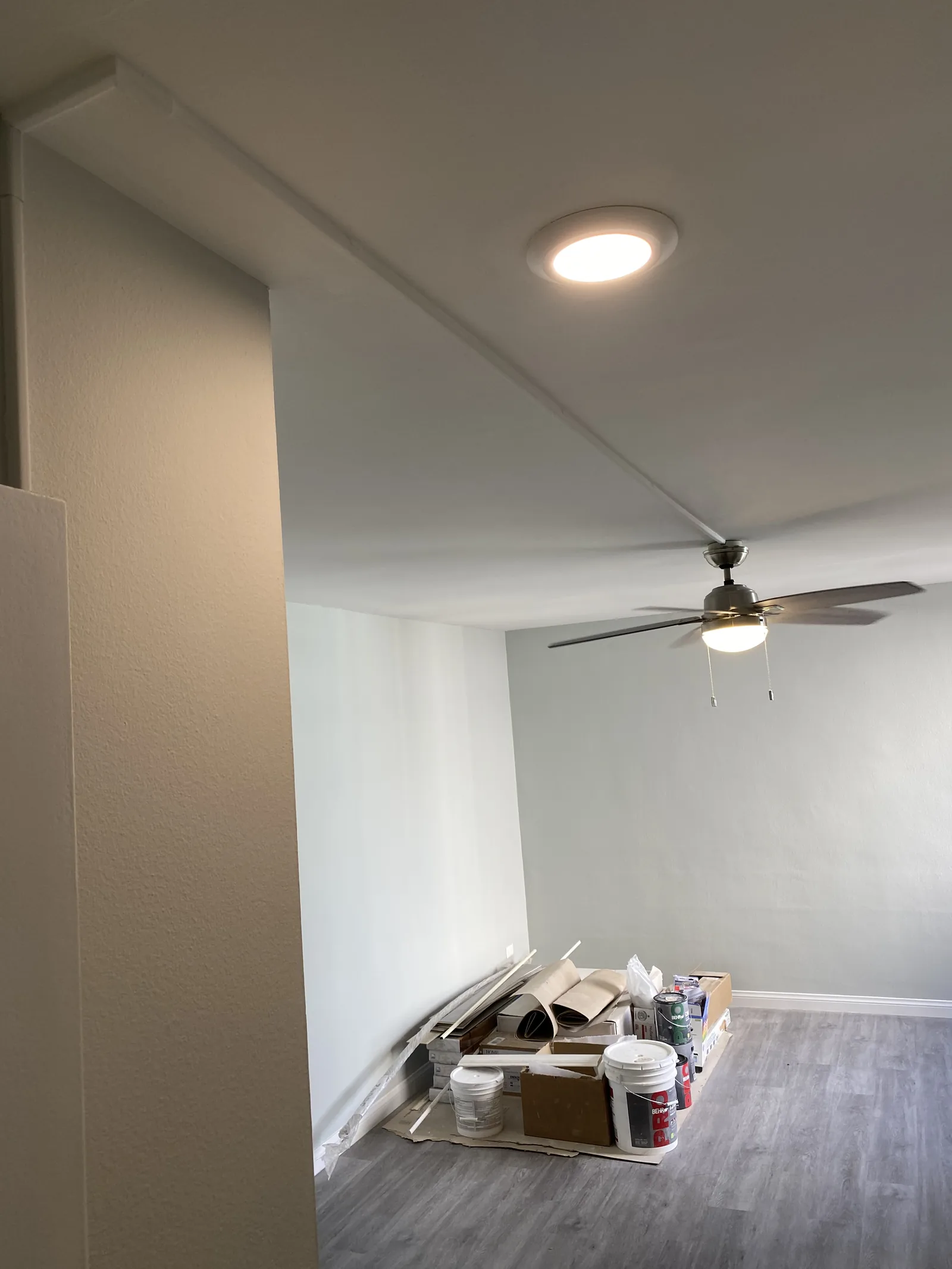 A second new ceiling fan and recessed light installed, with flooring materials staged below