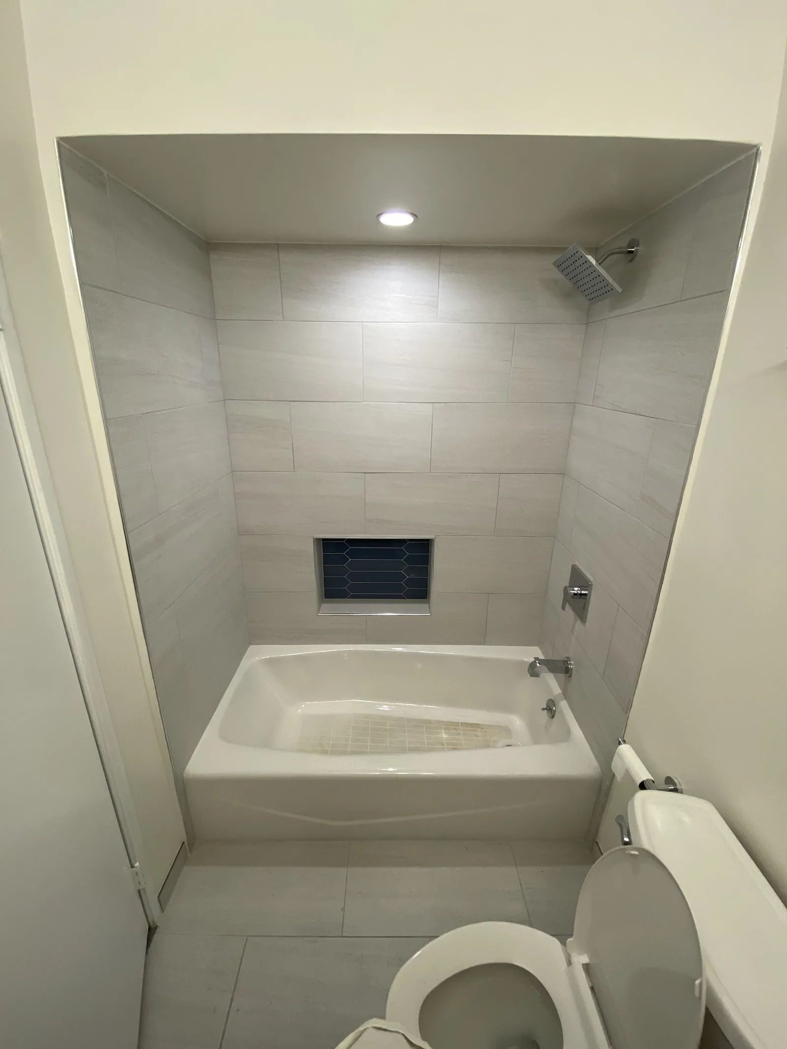 The finished first bathroom with a tiled tub surround, recessed light, and new toilet